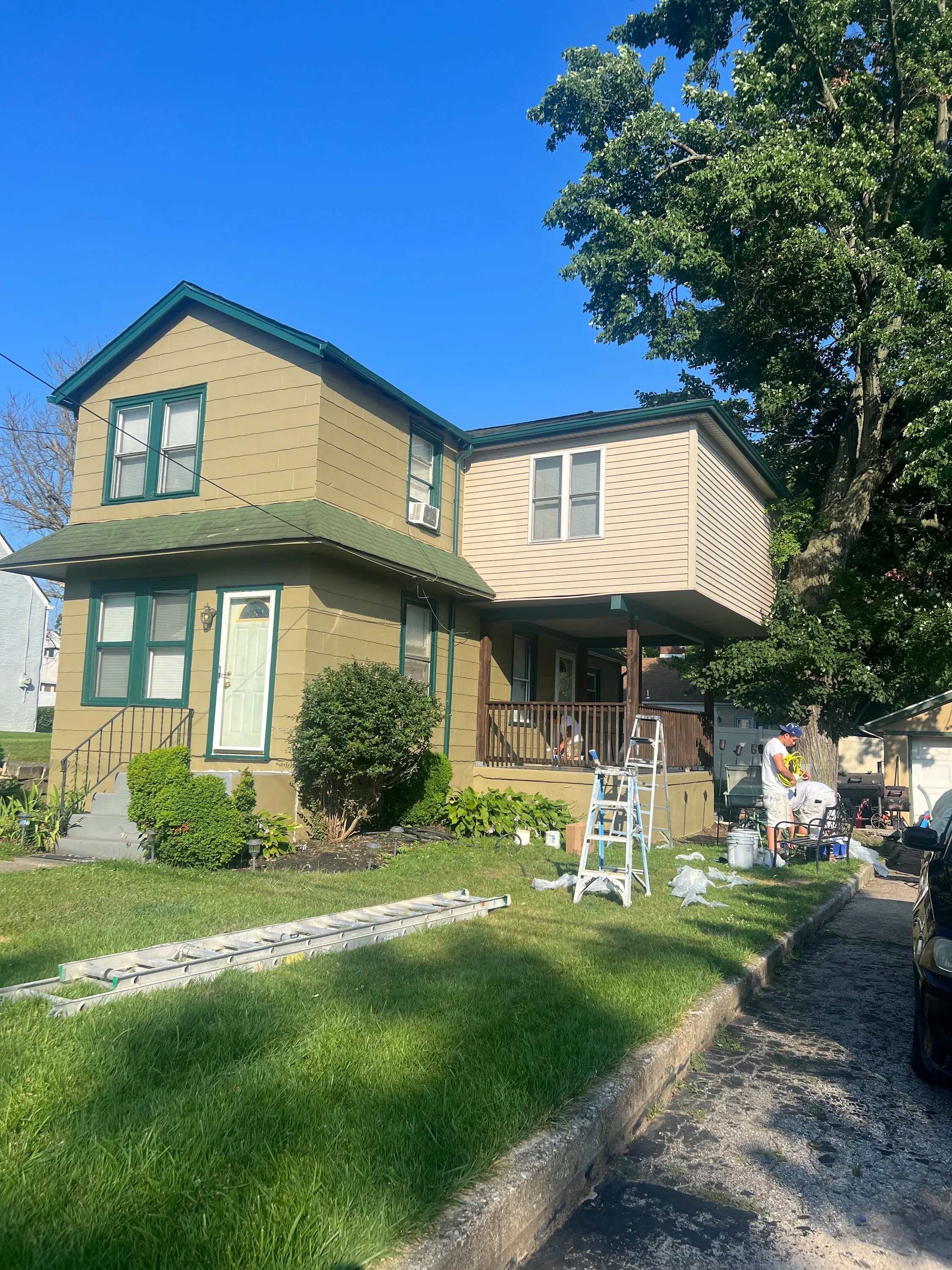 Olive 2-story Pennsylvania colonial mid-repaint with fresh cream addition, drop cloths on the driveway, two-person JL crew on site