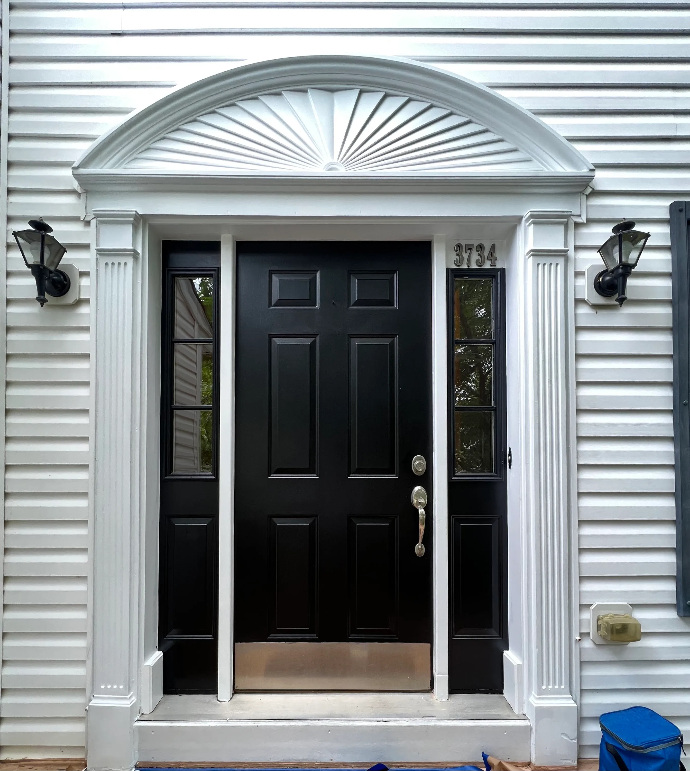 Same front door after JL refinish — premium deep black 6-panel under sunburst pediment, white columns and trim, 3734 address