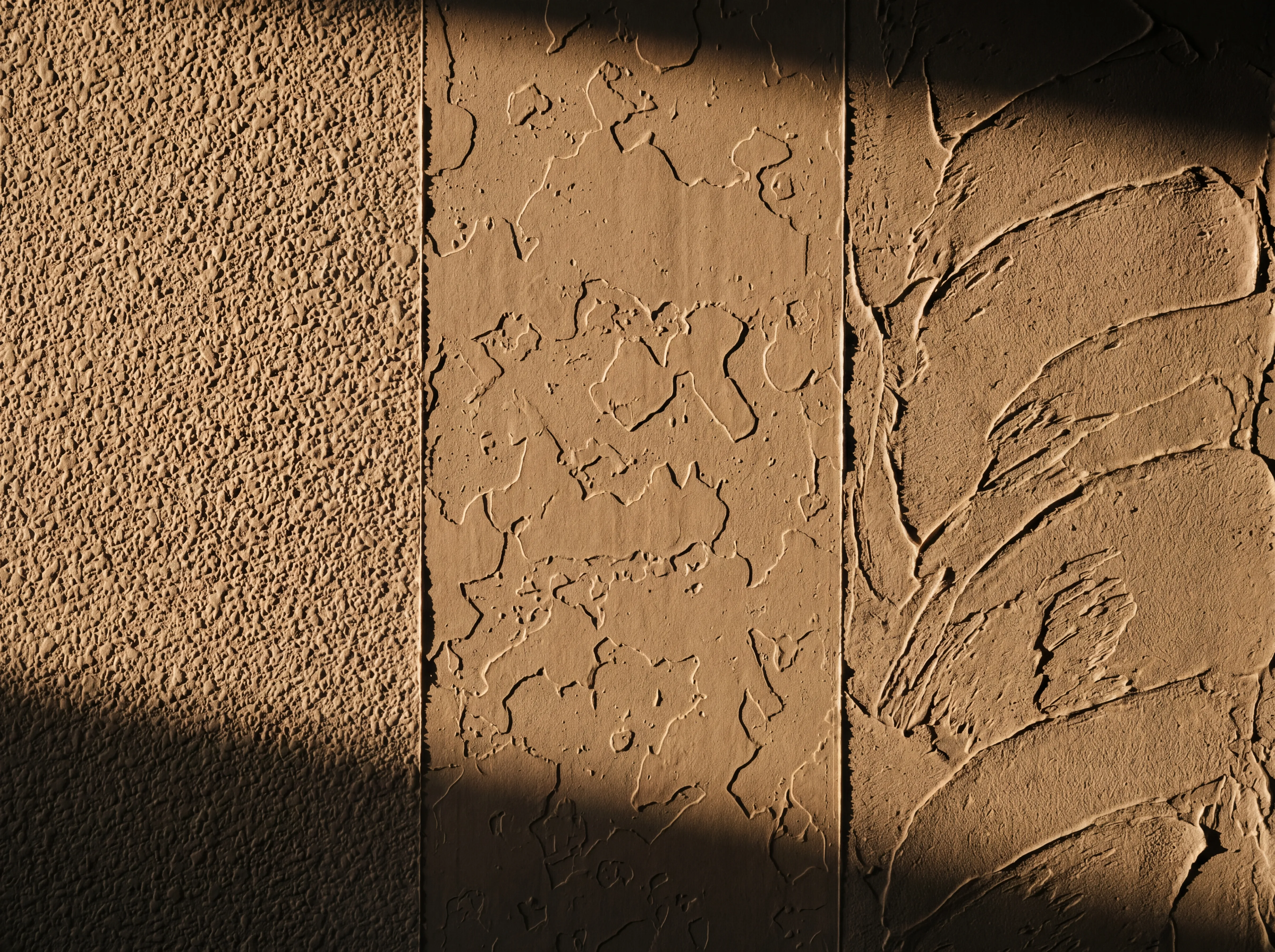 Three drywall texture sample sections side by side on one wall — orange peel on the left, knockdown in the middle, skip-trowel on the right — raking sidelight reveals each pattern